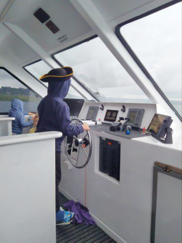 Kid given the opportunity to steer the boat on the way back from Lake Taupo Maori Rock Carving Cruise