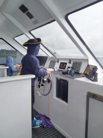 Kid given the opportunity to steer the boat on the way back from Lake Taupo Maori Rock Carving Cruise